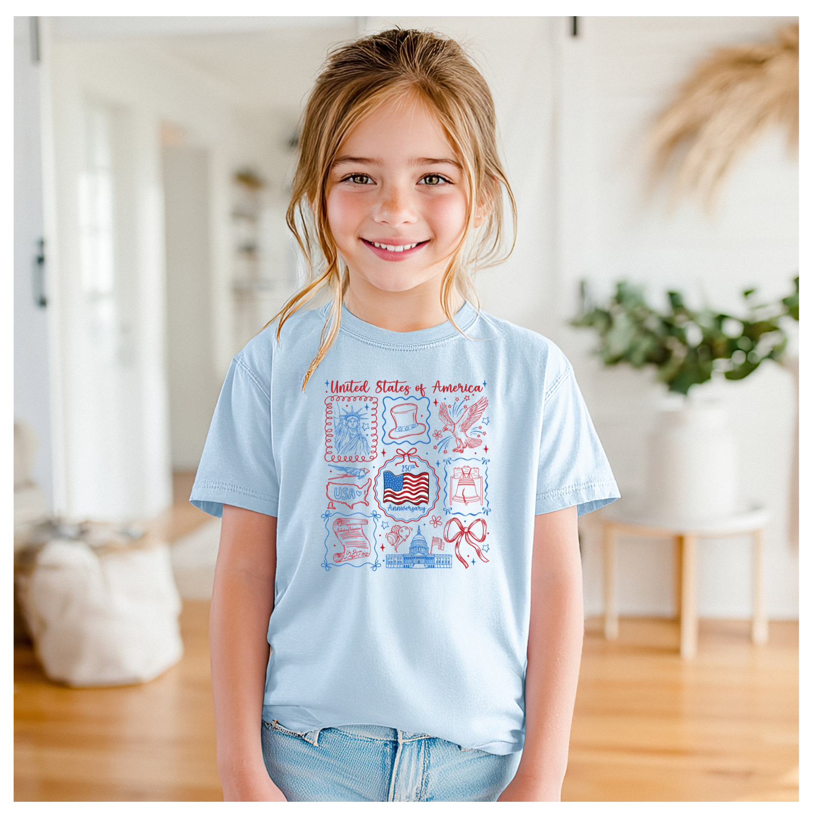 Young girl wearing a light blue t-shirt with a graphic design, standing in a room with wooden flooring and white walls.